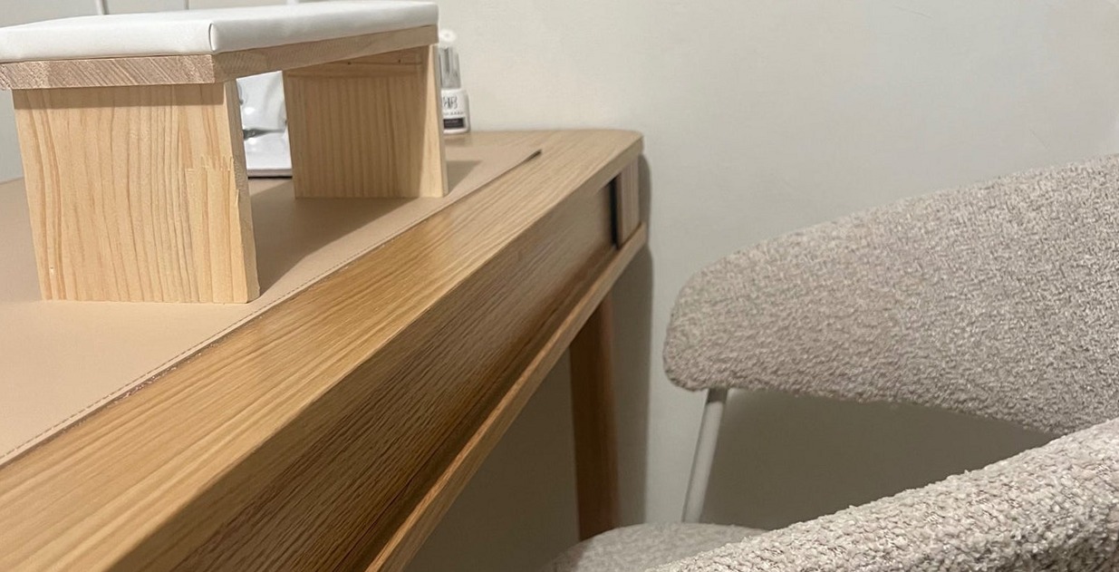 De nageltafel van lichtgekleurd hout met een handsteun en een bouclé stoel